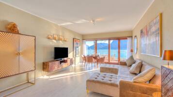 A modern living room with a sofa, television, and dining area with a view of the sea.