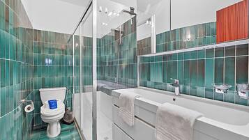 A modern bathroom with a glass shower enclosure, a toilet, and a white bathtub with a large mirror above it.