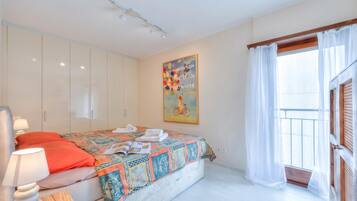 A bedroom with a bed, a nightstand, a lamp, a painting, and a window with curtains.