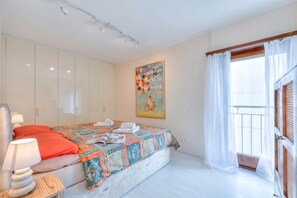 A bedroom with a bed, a nightstand, a lamp, a painting, and a window with curtains. - Emotion Lake Lugano With Direct Lake Access and Shared Pool (Mendrisio)