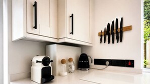 Una cocina con gabinetes blancos, una cafetera, un hervidor y un mueble para cuchillos.