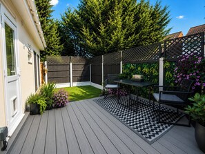 A deck with a checkered floor, a table with chairs, and a garden area with a fence and plants.