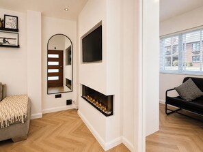 A modern living room with a fireplace, a sofa, a TV mounted on the wall, and a large window.