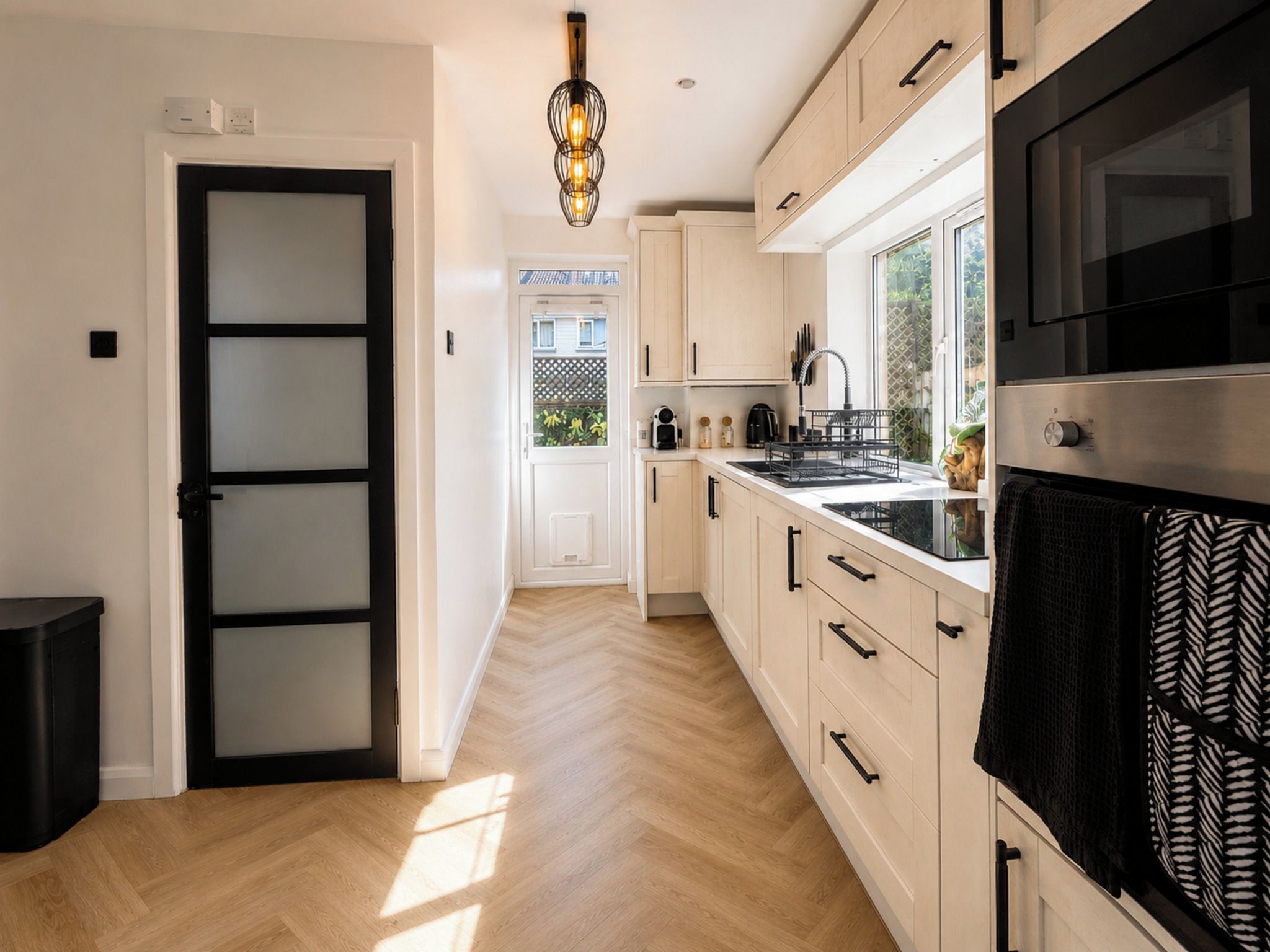 A modern kitchen with light wood cabinets, a black oven, and a window with a view of greenery.