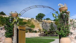 A paved pathway leading to a wooden gate, flanked by large terracotta pots with plants, under a clear blue sky. - Kouvaras Equestrian Club Residence by RHS (Kouvara)