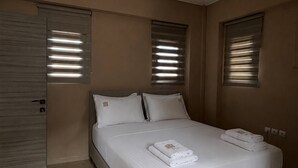 A modern bedroom with a large bed, built-in storage, and a sliding door. - Kouvaras Equestrian Club Residence by RHS (Kouvara)