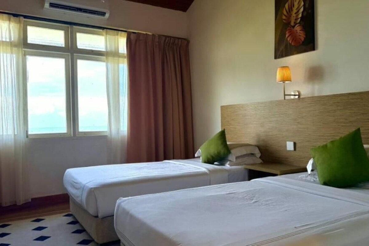 Habitación de hotel con dos camas, una ventana con cortinas, una lámpara de pared y un cuadro enmarcado.