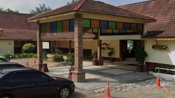 A building with a tiled roof, a covered entrance, and a sign with a bird logo. There are potted plants and a parked car. - Lilla Sea View Retreat Malacca (Alor Gajah)
