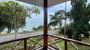 Un espacio al aire libre techado con terraza de madera, barandilla y vista al mar y a los árboles.