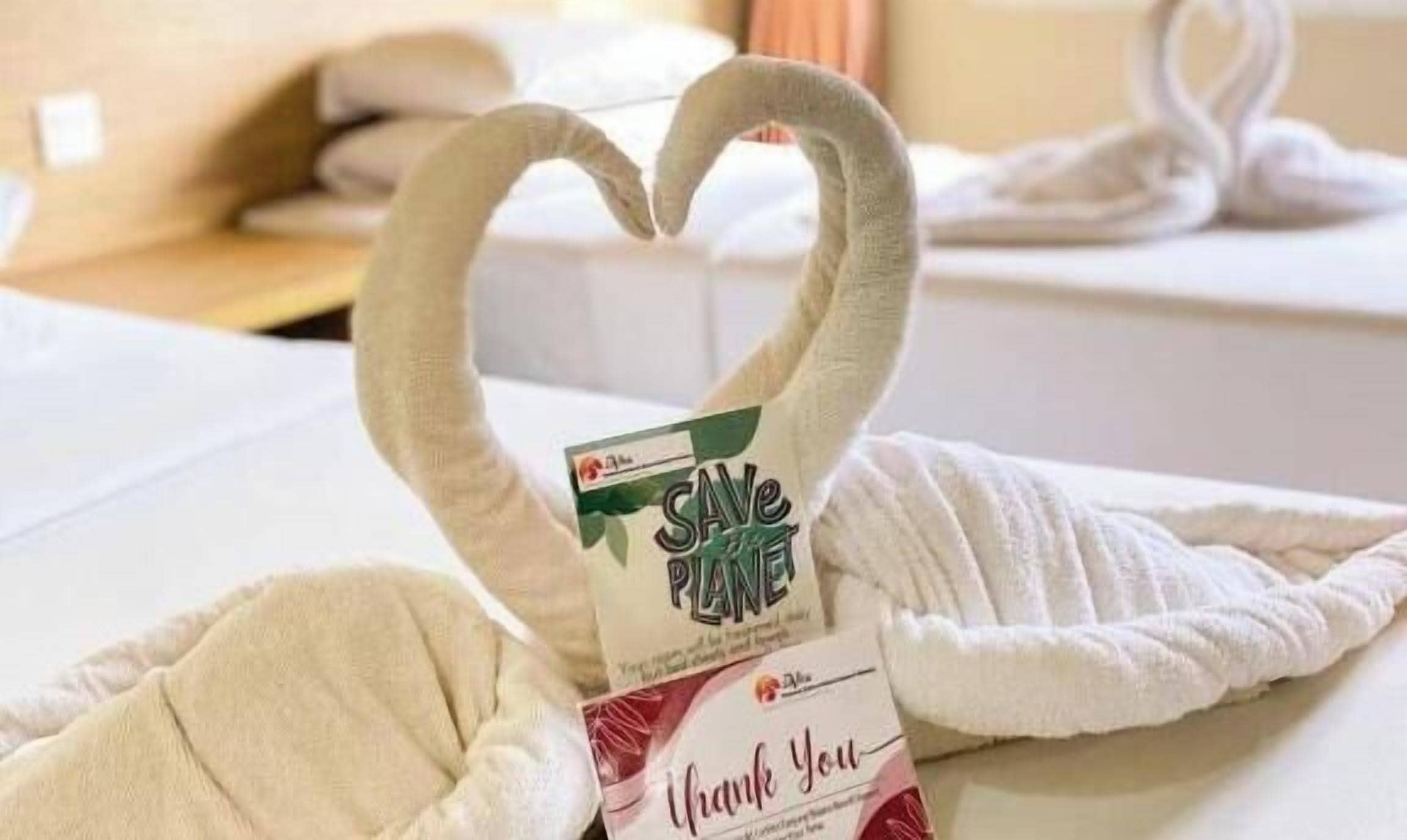 A towel with a heart shape and a card that reads 'SAVE PLANET' and 'Thank You' on a bed.