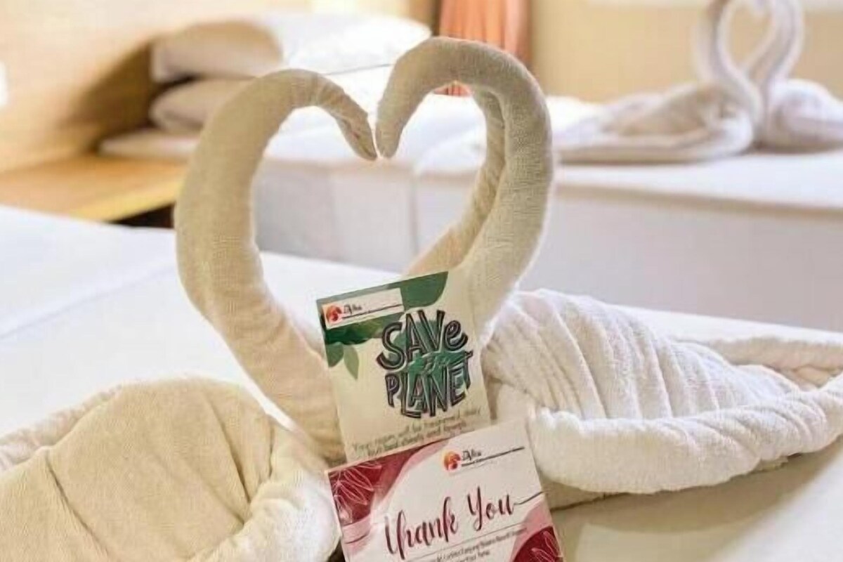 Una toalla con forma de corazón y una tarjeta que dice 'SAVE PLANET' y 'Gracias' sobre una cama.