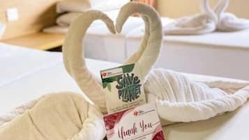 A towel with a heart shape and a card that reads 'SAVE PLANET' and 'Thank You' on a bed.