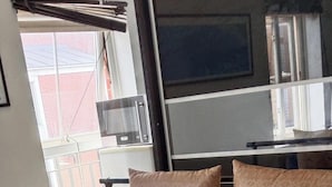 A bed with checkered bedding, a rolled white towel, and a view of the outside through a window.