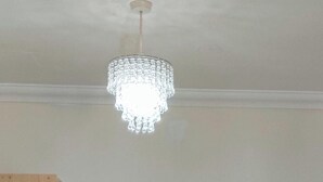 A room with a chandelier, a wooden wardrobe, a table with a white tablecloth, and a black office chair.