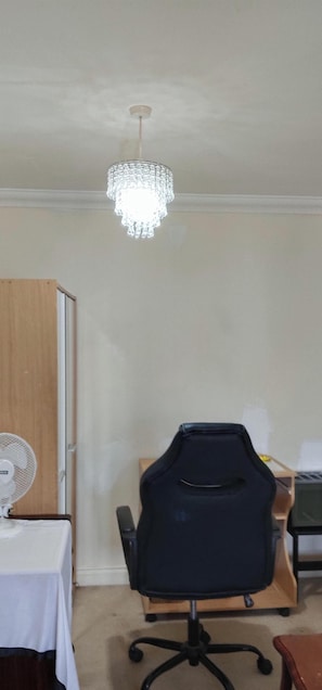 A room with a chandelier, a wooden wardrobe, a table with a white tablecloth, and a black office chair.