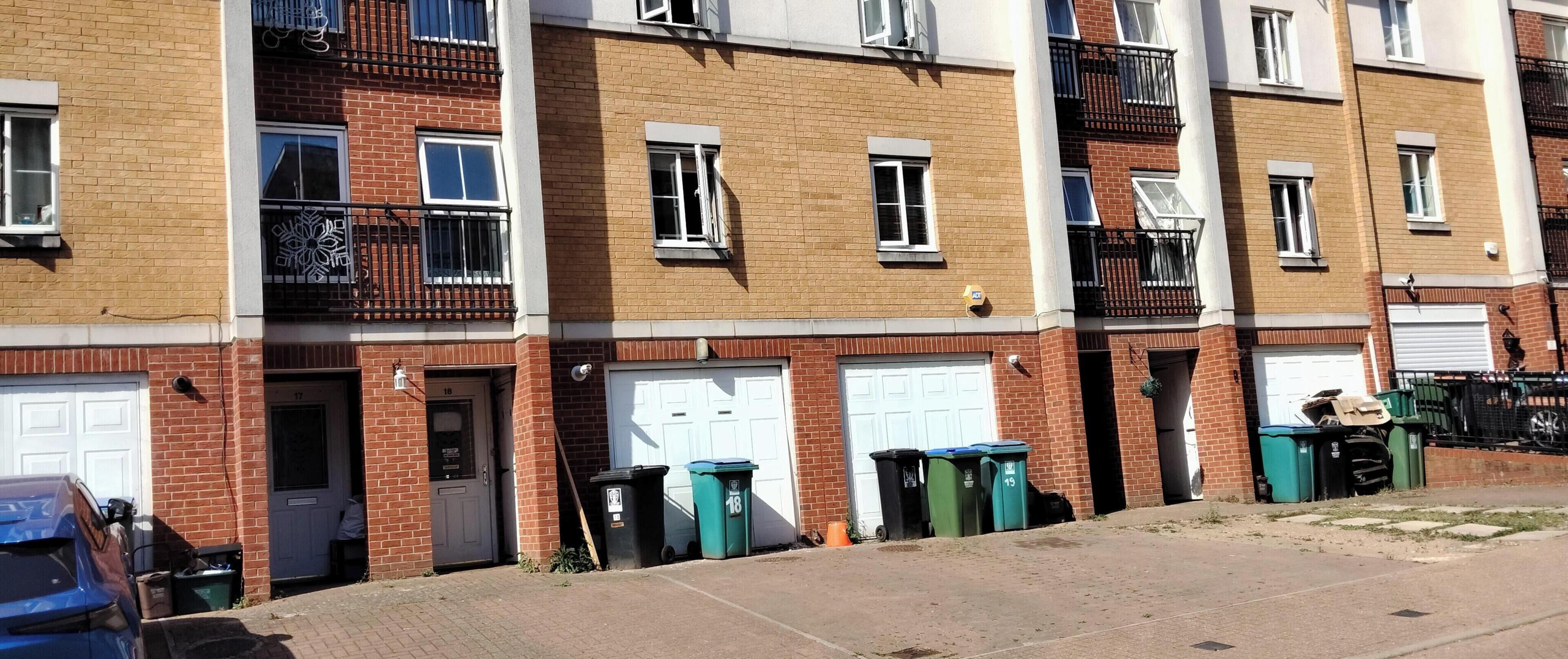 A row of townhouses with brick facades, white garage doors, and balconies with black railings.