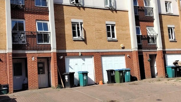 A row of townhouses with brick facades, white garage doors, and balconies with black railings.