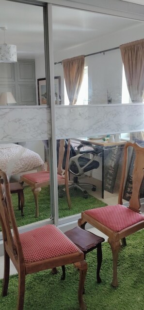 A room with a large mirror reflecting a bed, a desk, and a chair. There is a green carpet and a window with curtains. - The Greenway Retreat - Watford Home: 7BR, Nr London & Studios + Indian Cuisine (Watford)