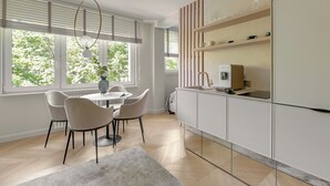 A modern kitchen with white cabinetry, a dining area with a glass table and chairs, and a view of greenery through the windows. - The Secret Escape - Close to the Beach (Sopot)