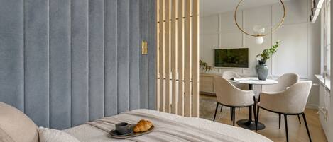 A modern bedroom with a bed, a dining area with a table and chairs, and a large window.
