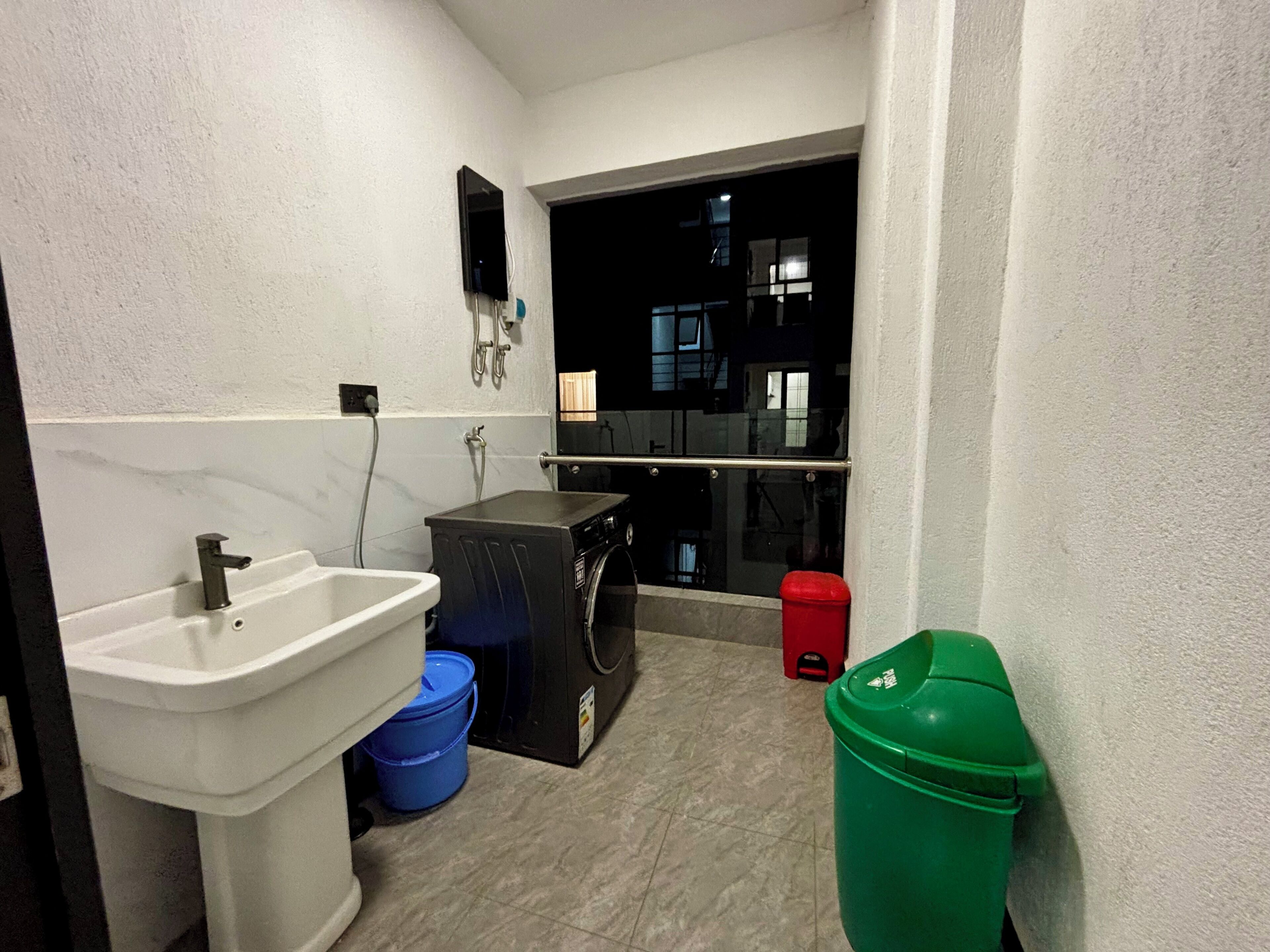 Un baño pequeño con un lavamanos, lavadora y un bote de basura.