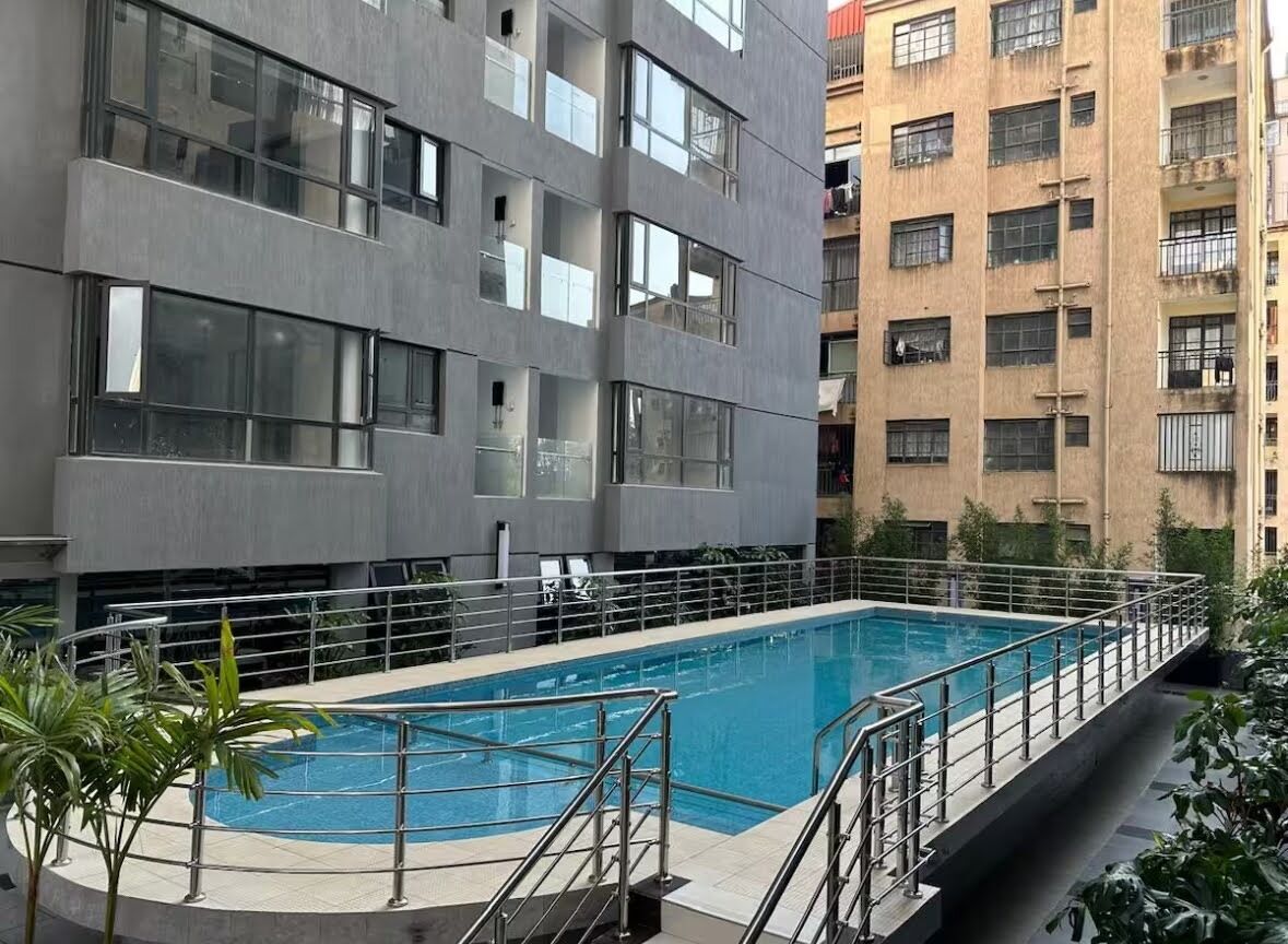 Piscina no terraço com guarda-corpo metálico, cercada por um edifício com janelas amplas e varandas.