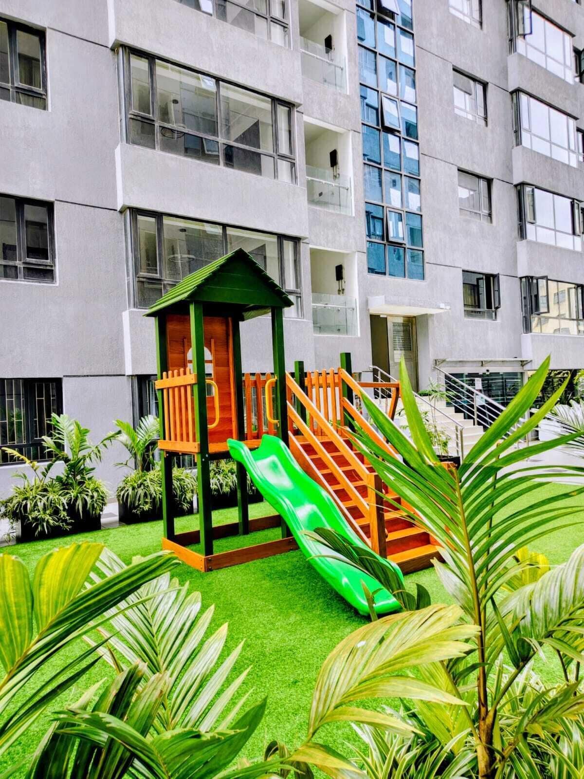 Edifício com vários andares e área de recreação infantil, com escorregador e estrutura de escalada.