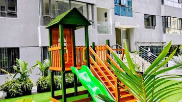 Edifício com vários andares e área de recreação infantil, com escorregador e estrutura de escalada.