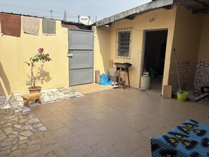 A courtyard with a tiled floor, a potted plant, a bench, a gate, and a satellite dish. - Single-story house with an inner courtyard, ideal for a family (Abidjan)