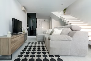 A modern living room with a grey sofa, a TV on a wooden cabinet, and a black and white patterned rug. - Elegant and comfortable triplex in Chamartín (Madrid)
