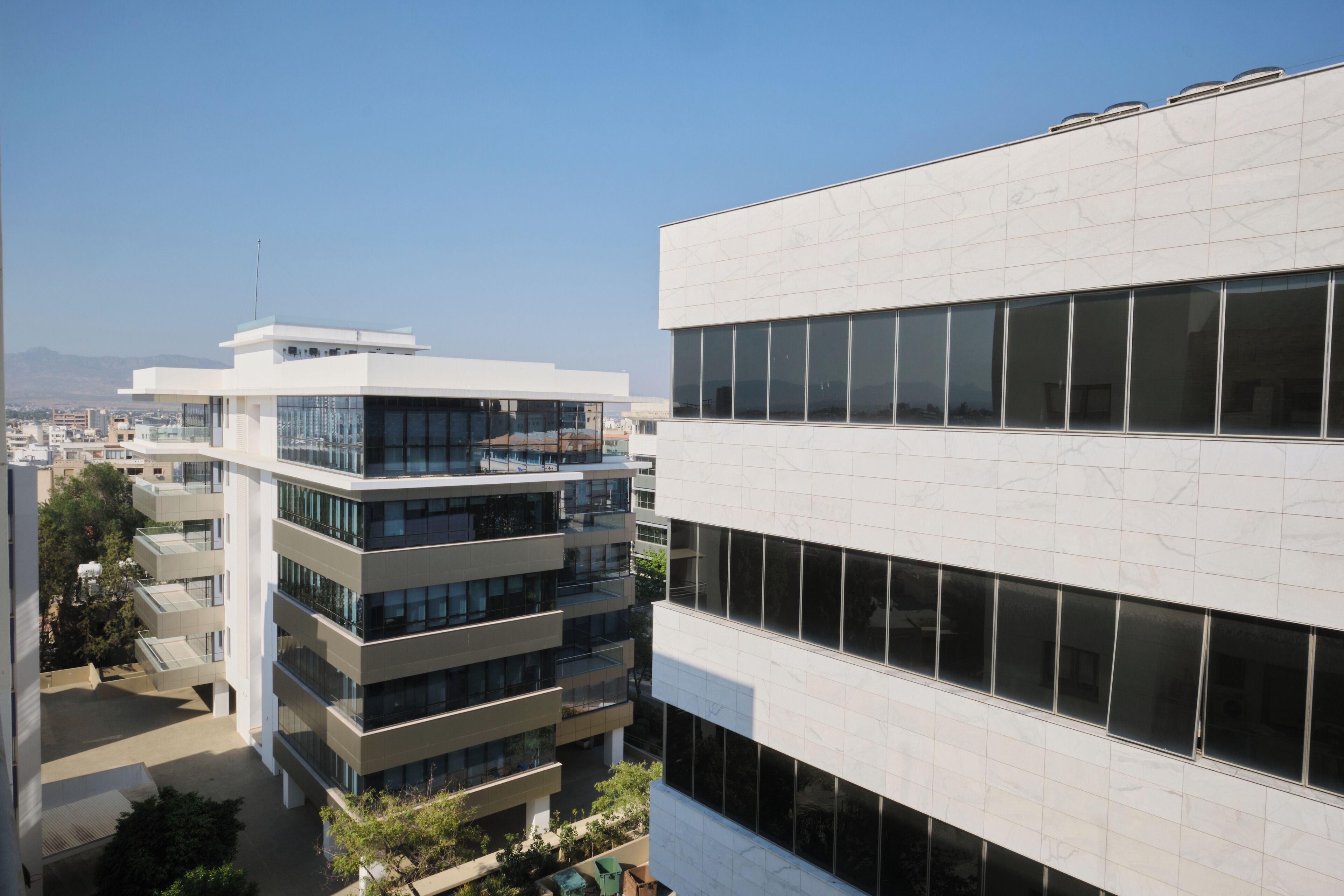 A modern building with multiple floors and large windows, surrounded by other buildings and greenery.