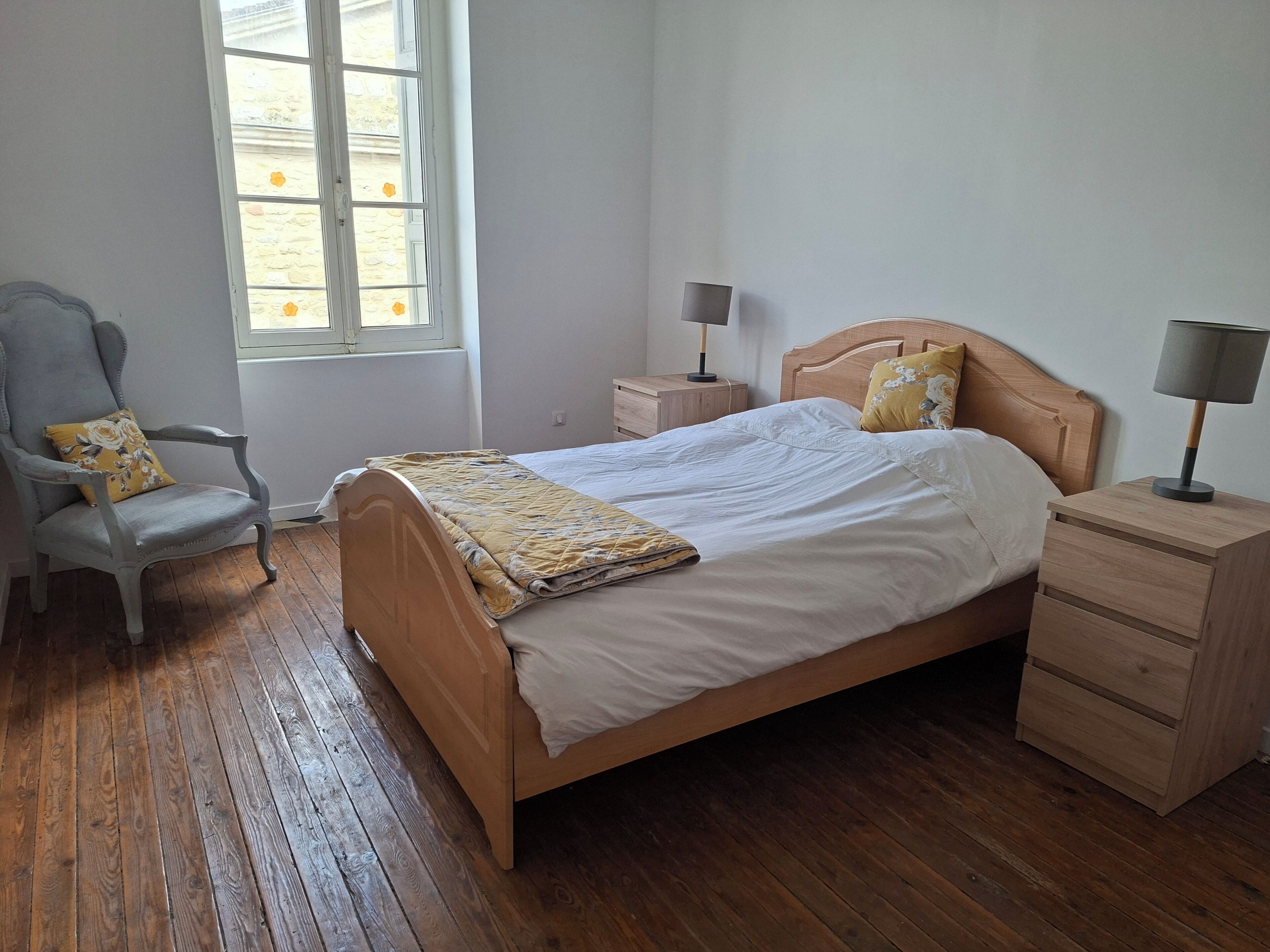Une chambre à coucher avec un lit en bois, une chaise, une table de chevet et une fenêtre.