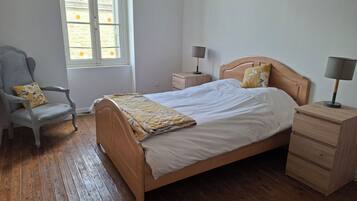 A bedroom with a wooden bed, a chair, a nightstand, and a window.