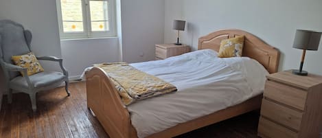 Un dormitorio con cama de madera, una silla, una mesita de noche y una ventana.