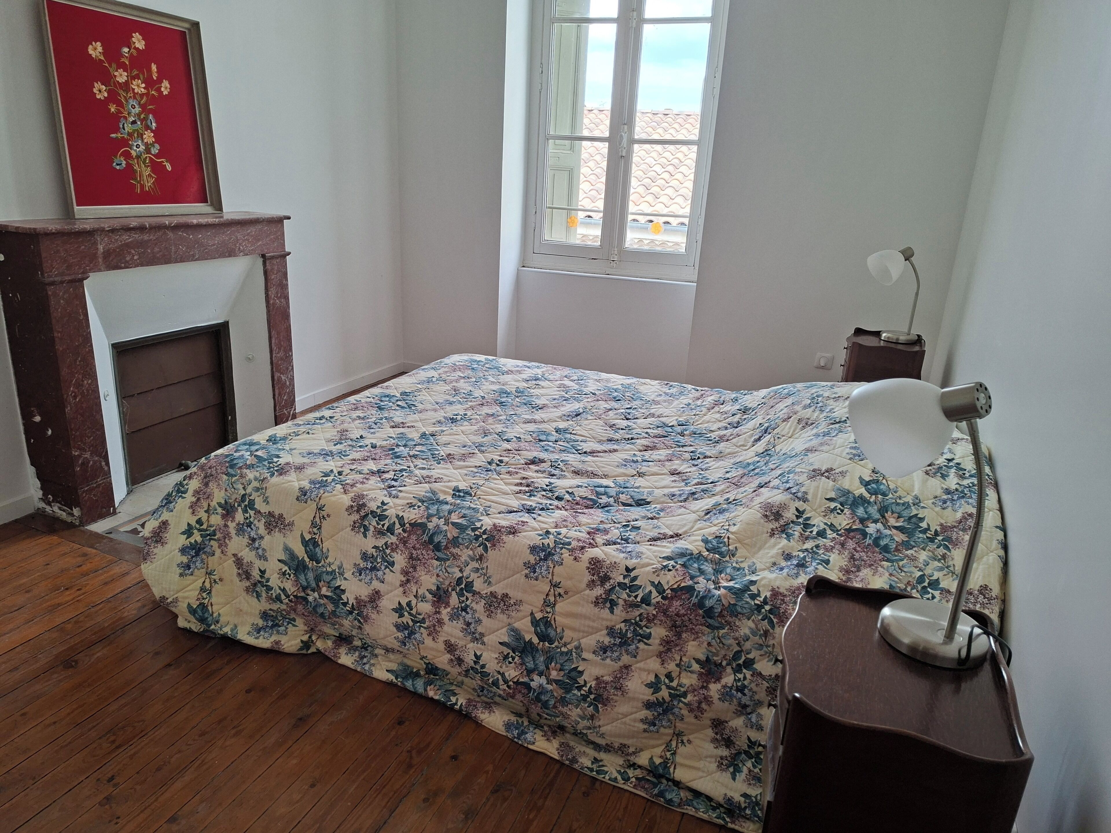Una camera da letto con una coperta a fiori, un camino, una finestra vista e una scrivania con una lampada.