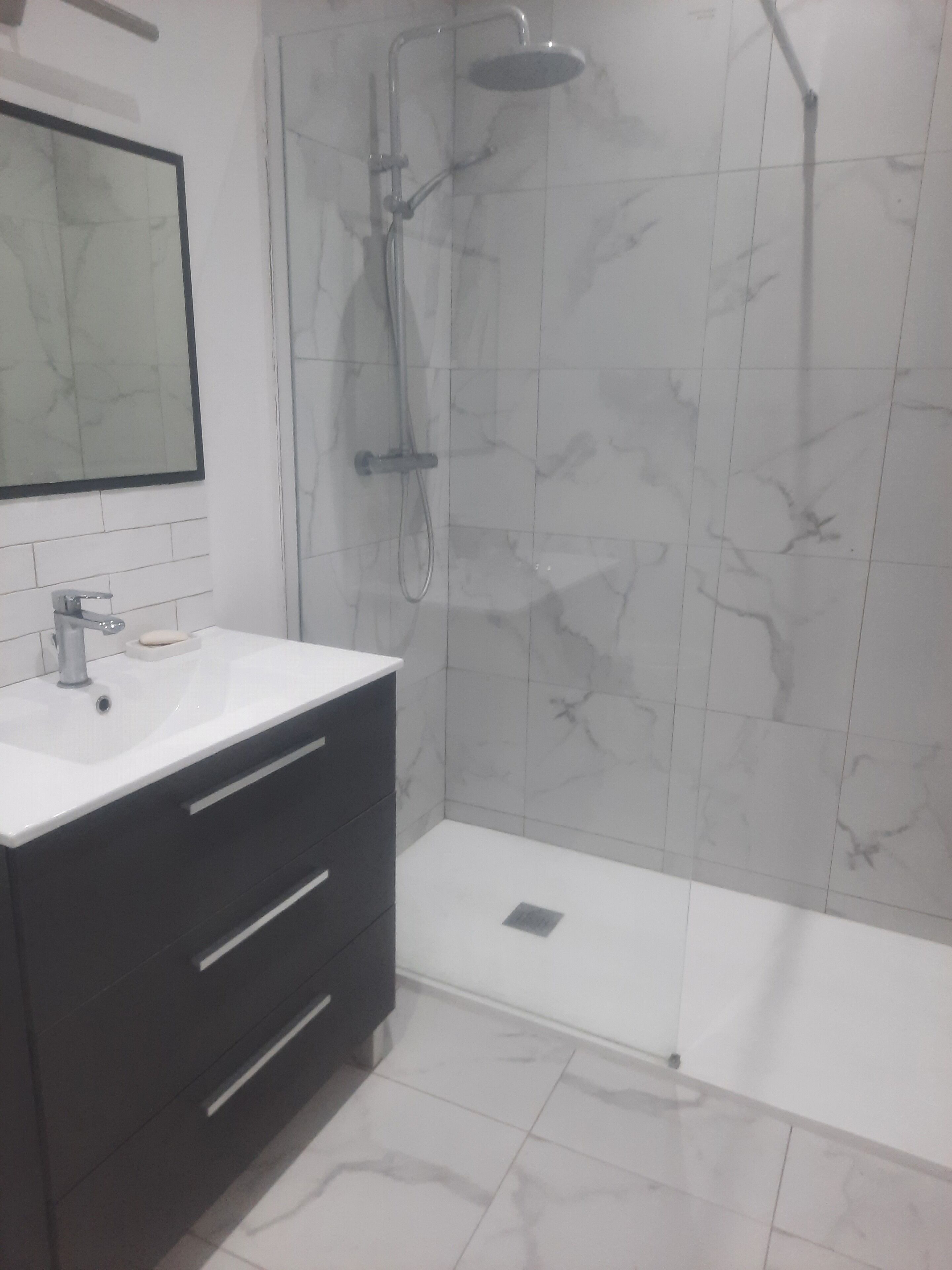 Une salle de bain avec un lavabo blanc, un meuble sombre et un espace douche doté d’une porte en verre.