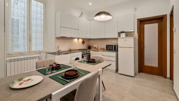 A modern kitchen with white cabinets, a dining table set with plates and glasses, and a microwave. - [CasadiCavour]5Terre/reach everything by foot +A/C (La Spezia)