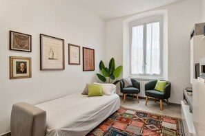 Ein modernes Schlafzimmer mit einem Bett, zwei Stühlen, einem großen Fenster und gerahmten Bildern an der Wand.