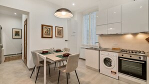 A modern kitchen with a built-in washing machine, a dining area with a table and chairs, and a pendant light. - [CasadiCavour]5Terre/reach everything by foot +A/C (La Spezia)