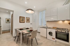 A modern kitchen with a built-in washing machine, a dining area with a table and chairs, and a pendant light. - [CasadiCavour]5Terre/reach everything by foot +A/C (La Spezia)