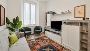 A modern living room with a sofa, two armchairs, a flat-screen TV, a bookshelf, and a large window with curtains. - [CasadiCavour]5Terre/reach everything by foot +A/C (La Spezia)