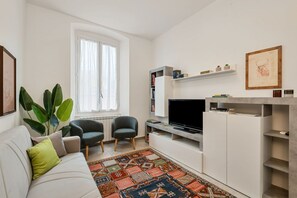 A modern living room with a sofa, two armchairs, a flat-screen TV, a bookshelf, and a large window with curtains. - [CasadiCavour]5Terre/reach everything by foot +A/C (La Spezia)