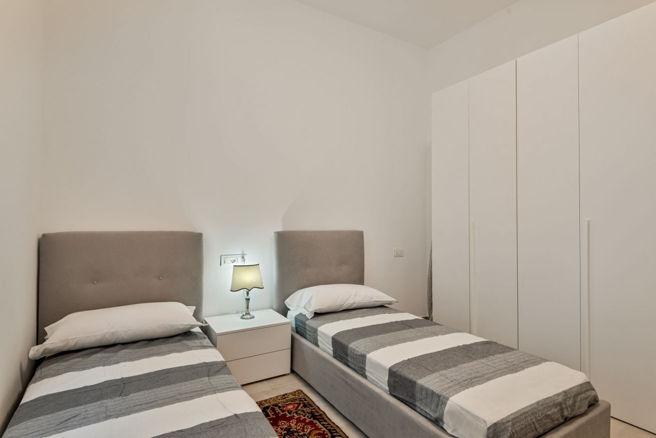 Un dormitorio con dos camas, una mesita de noche con lámpara y un armario.