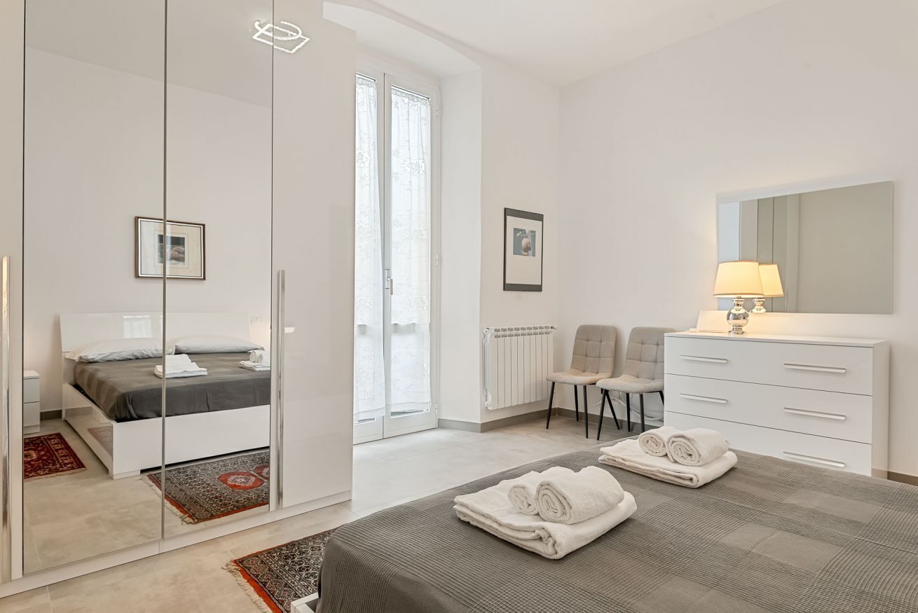 A modern bedroom with a bed, a dresser, a chair, and a mirror.