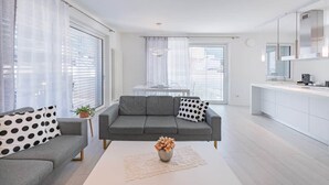 A modern living room with a grey sofa, a coffee table with a vase, and a kitchen area with white cabinets. - Talvera Penthouse—125 square meters with garage in downtown Bolzano (Bolzano)