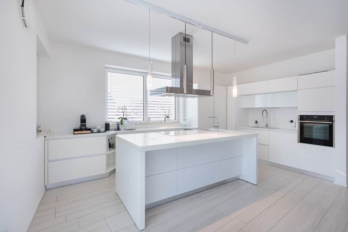 A modern kitchen with a central island, white cabinetry, and a stainless steel range hood.