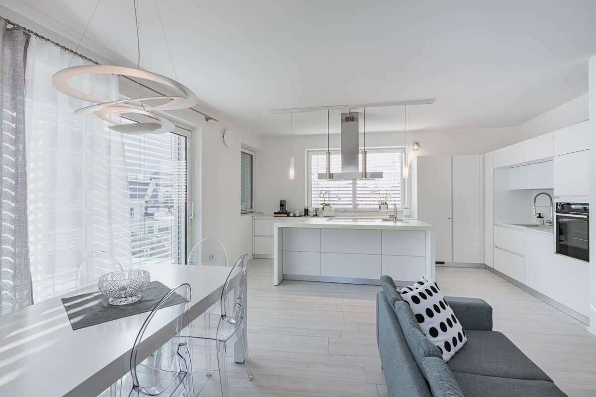 A modern kitchen with a central island, a dining area with a glass table, and a sofa with a patterned pillow.