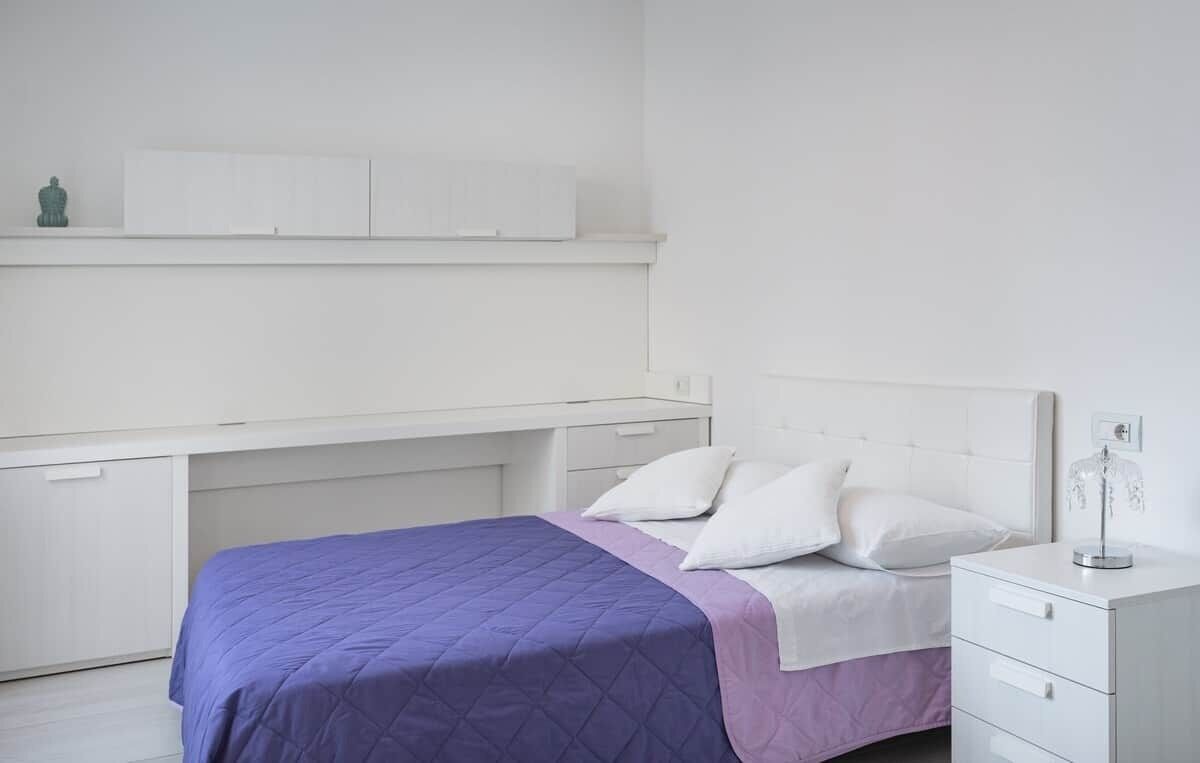 A bedroom with a bed, a nightstand, a dresser, and a shelf above the bed.