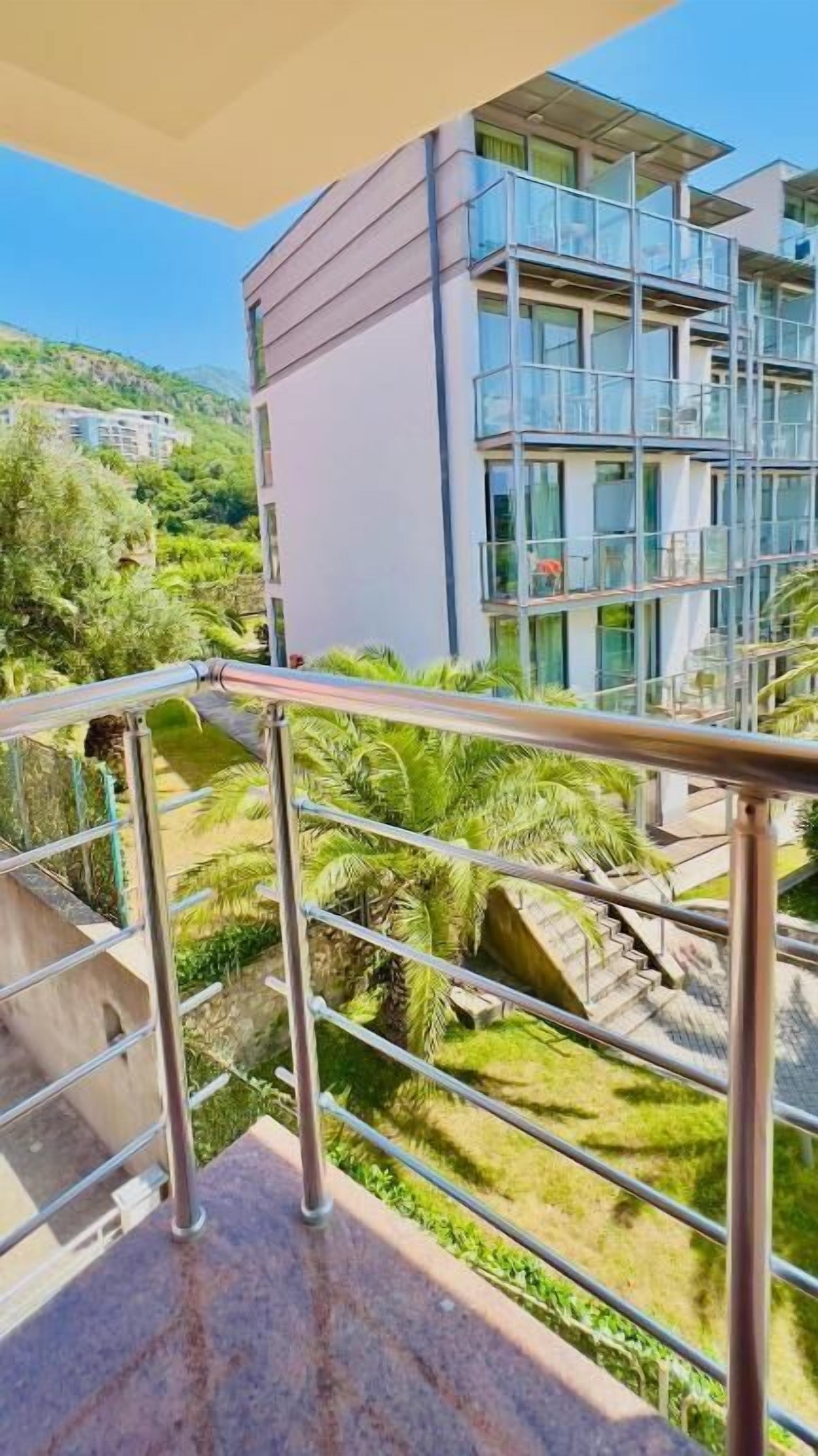 Un edificio moderno con balcón, rodeado de vegetación y un cielo despejado.
