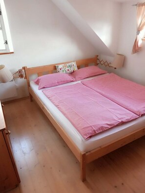 A single-bed room with a sloped ceiling, a wooden headboard, a bedside lamp, and a patterned pillow.